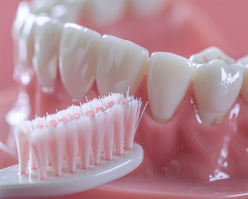 Closeup of a pink standard toothbrush next to a set of dentures with a pink background