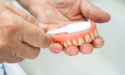 Someone brushing removed dentures in their hands with a white brush