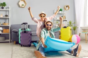 Man and woman in living room with suitcases and beach gear smiling